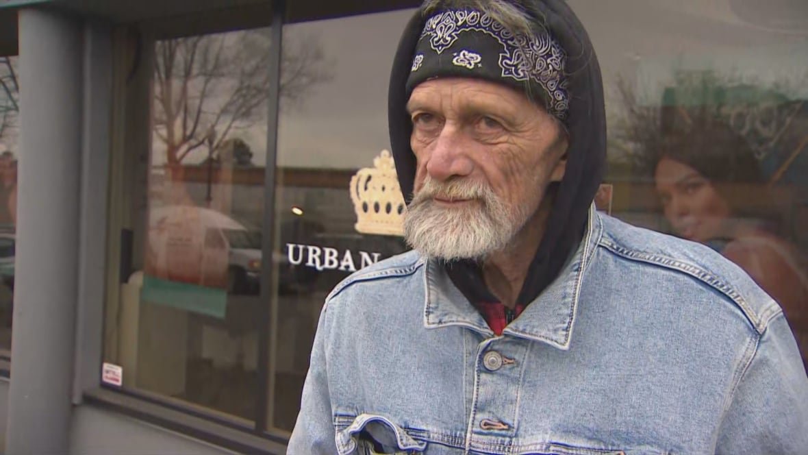A man wearing a hood and a bandana stands outside a store.