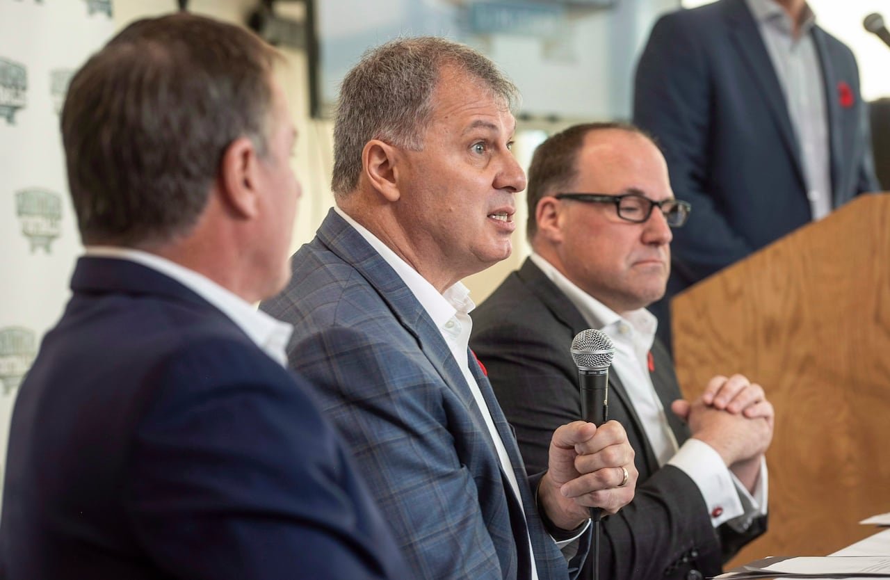Three individuals in suits at a press conference.