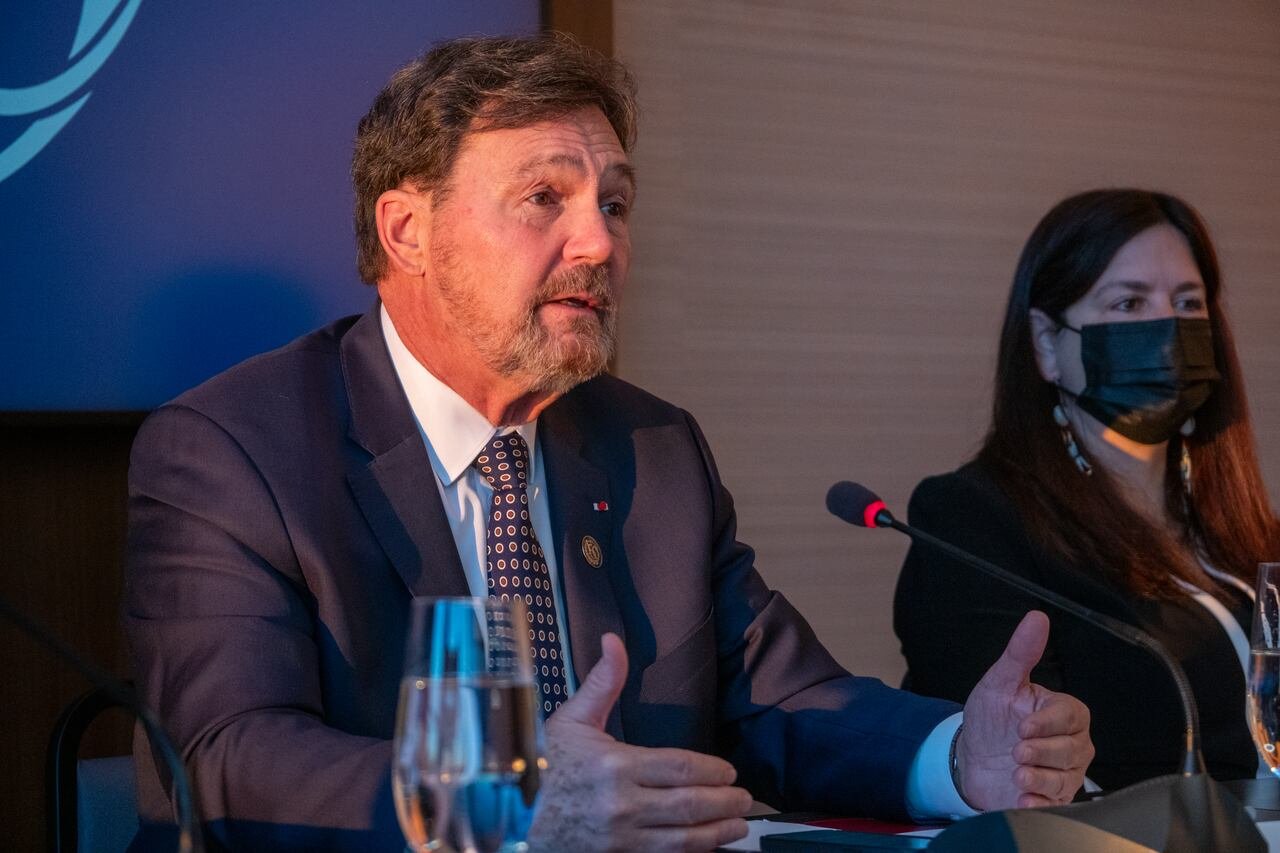 A person is seen sitting at a table, speaking into a microphone.