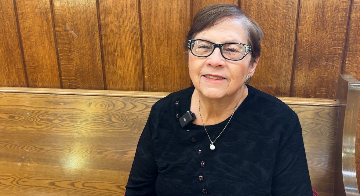 default-653 A woman in a black shirt and glasses sits on a wooden bench.