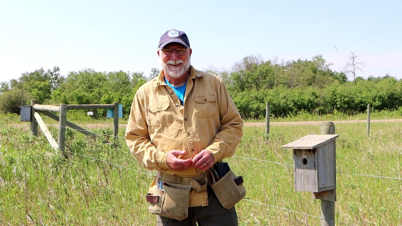 A man next to a wire fence with a wooden birdhouse attached.
