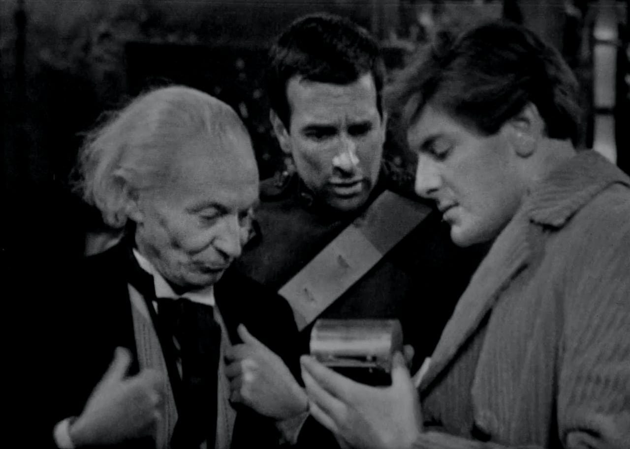 a black and white photo of 3 men standing looking at an object