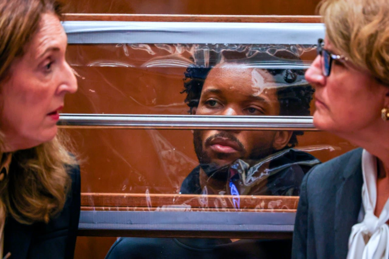 A man sits behind a plastic screen in a court room