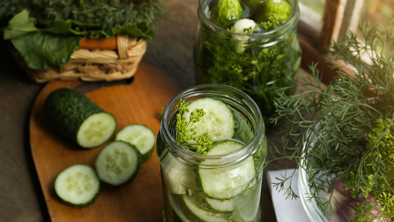 Closeup on glass jar of homemade pickles on a wooden cutting board.