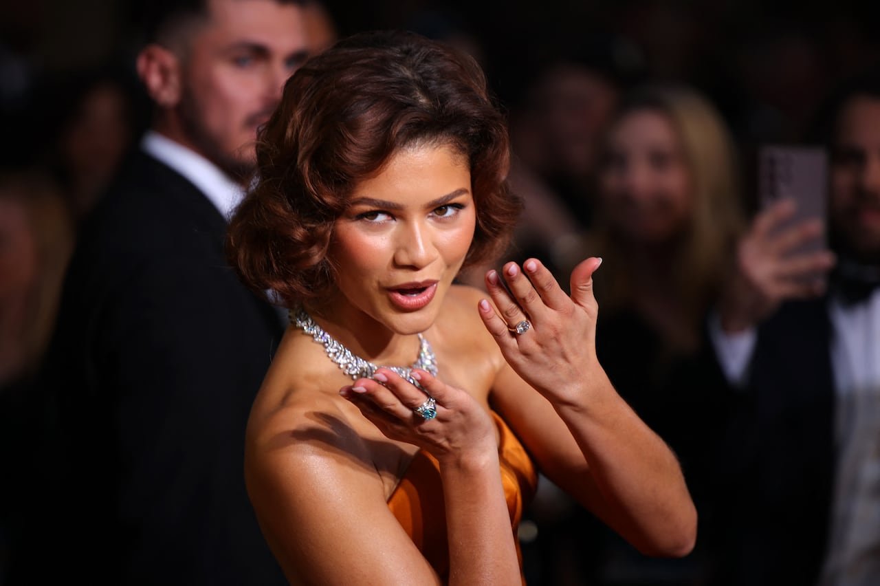 A woman blowing a kiss with diamond rings on both hands, wearing a large diamond necklace.
