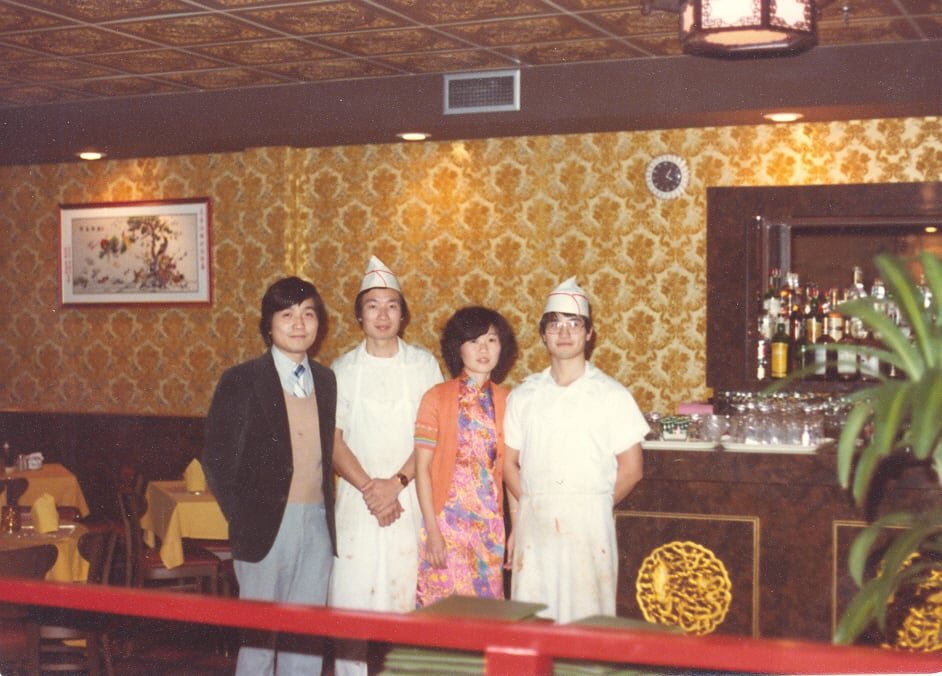A photo captured in 1979 portraying a man in formal attire, two chefs, and a woman in a restaurant setting.