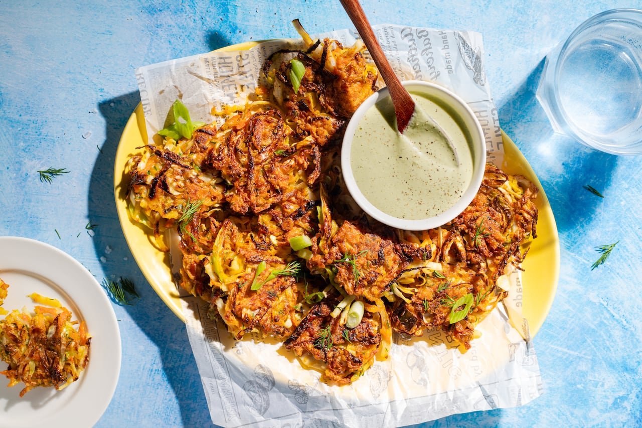 Top-down view of a platter of cabbage fritters with a small dish of yogurt dip on the side.