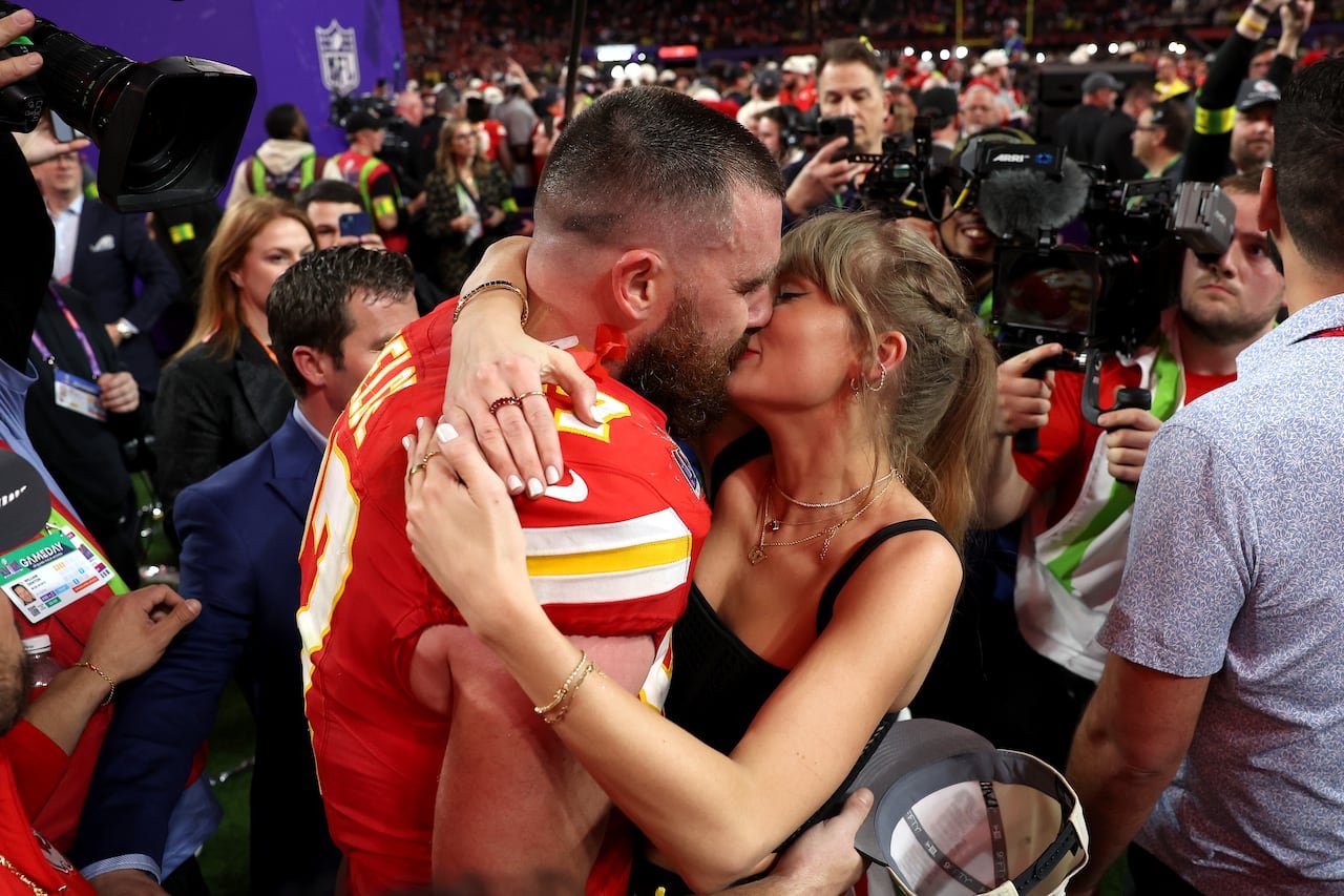 football player kissing woman in black tank top with ponytail amid a crowd on field