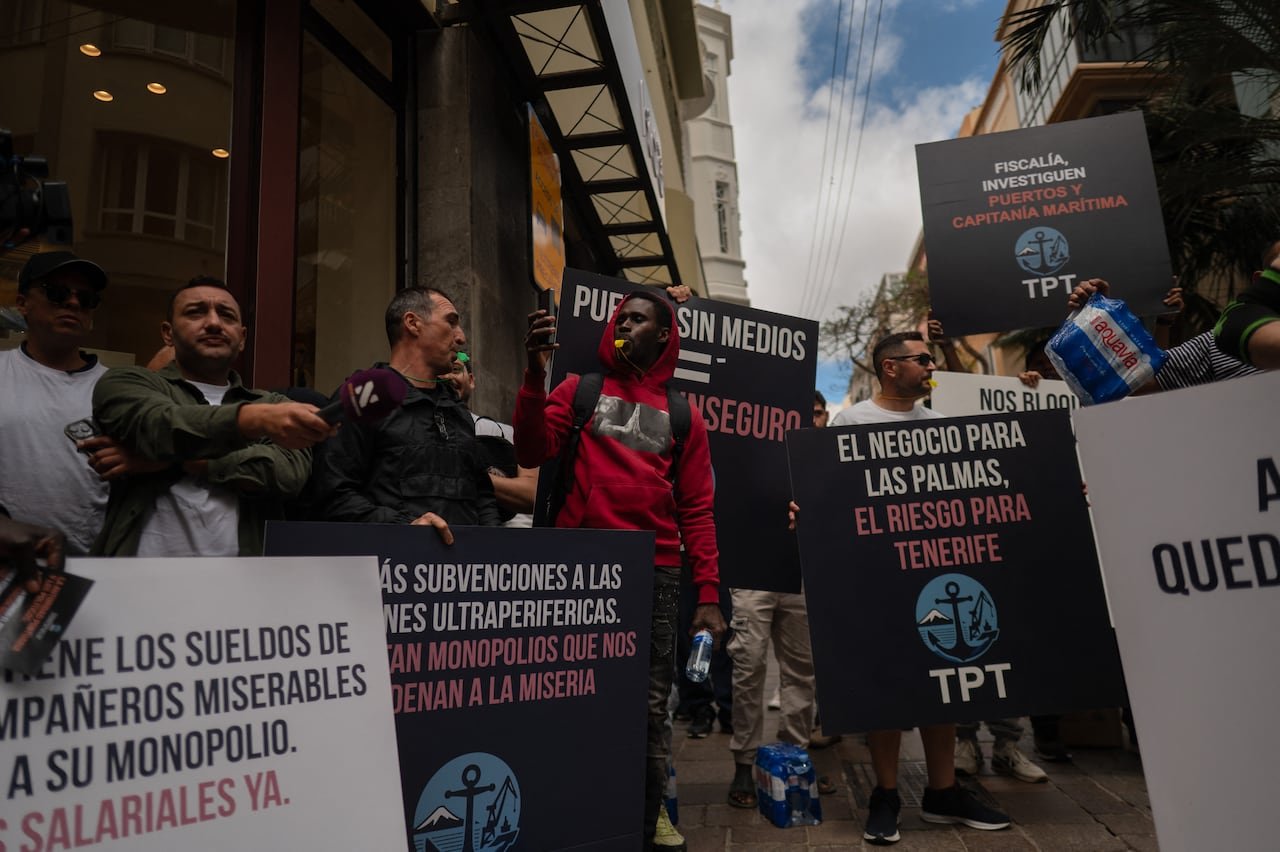 A group of men hold black and white protest signs with message written in Spanish.