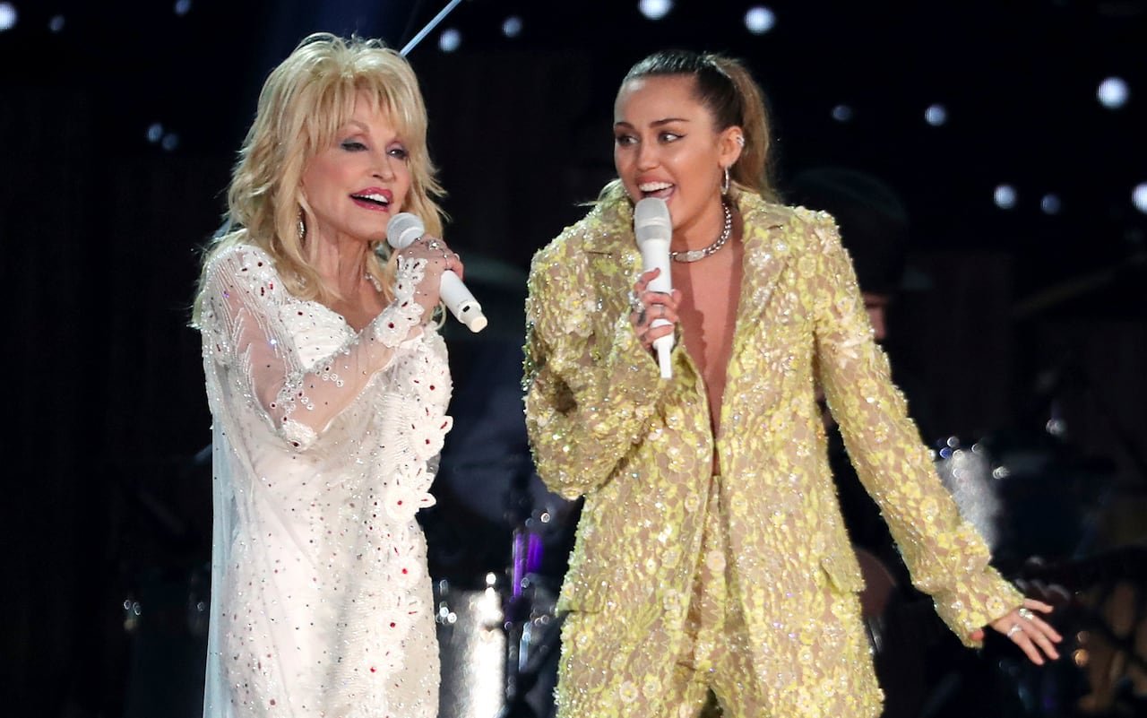 default-102 An older woman in a shiny white outfit sings onstage with a younger woman in a shiny gold outfit.