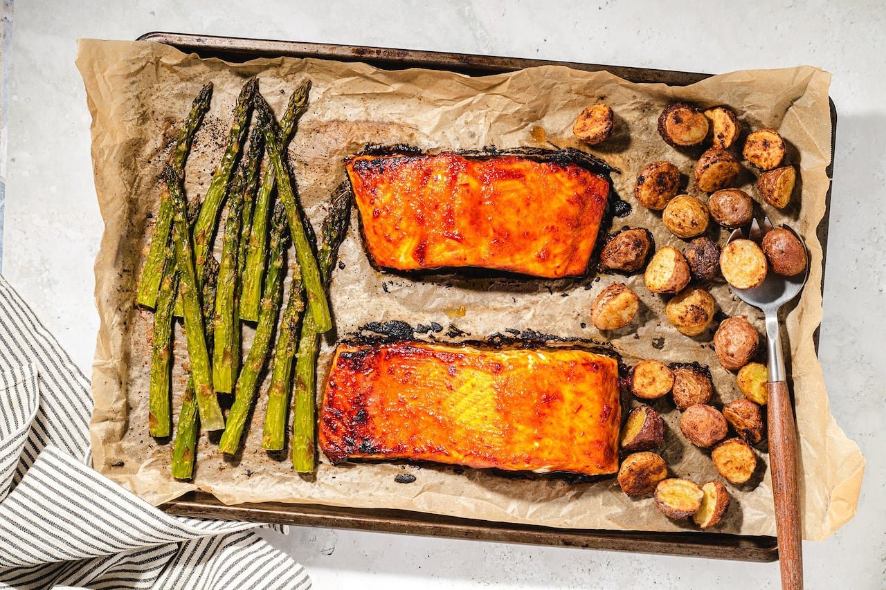 default-594 Top view of a baking sheet containing two baked salmon fillets, asparagus, and mini potatoes.