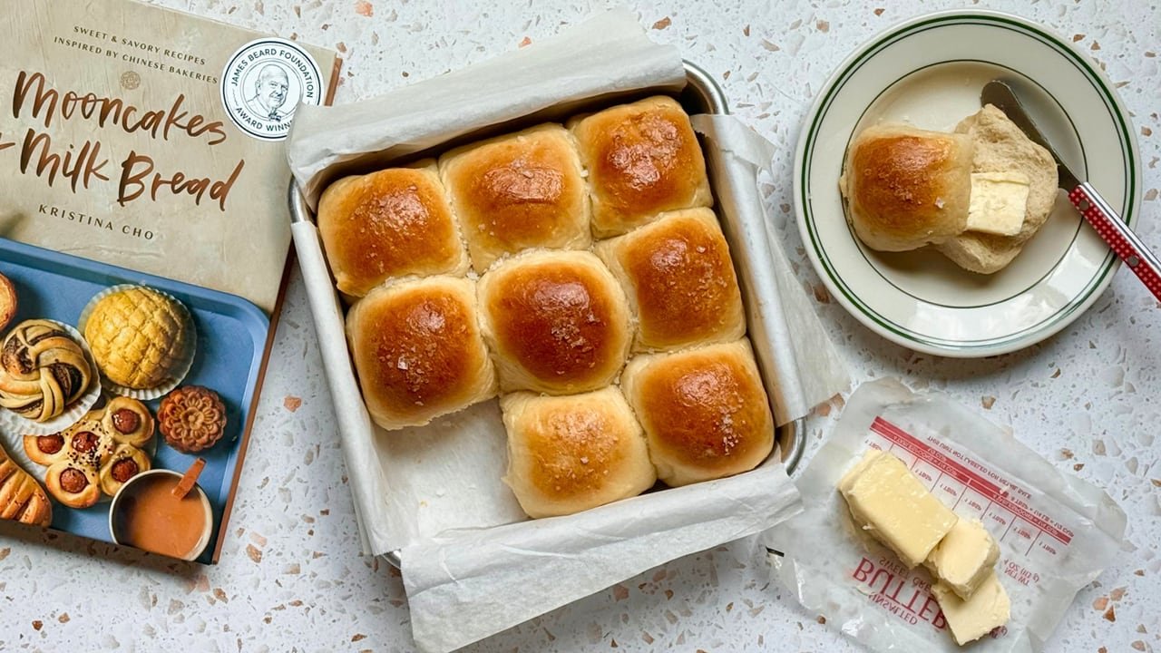 default-138 A square baking pan with freshly baked milk bread beside a copy of the cookbook, Mooncakes and Milk Bread, and a saucer of butter.