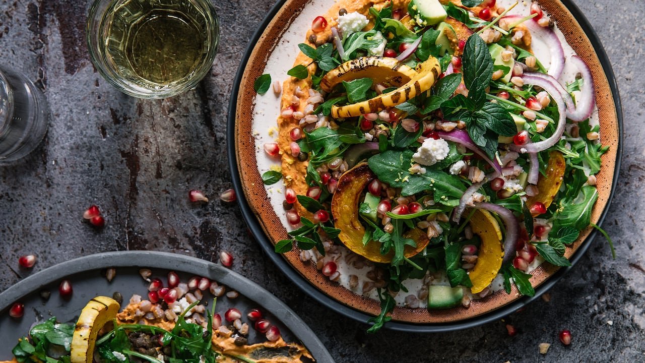 default-141 A large plate with a salad of delicata squash slices, herbs, onions, pomegranate and greens.